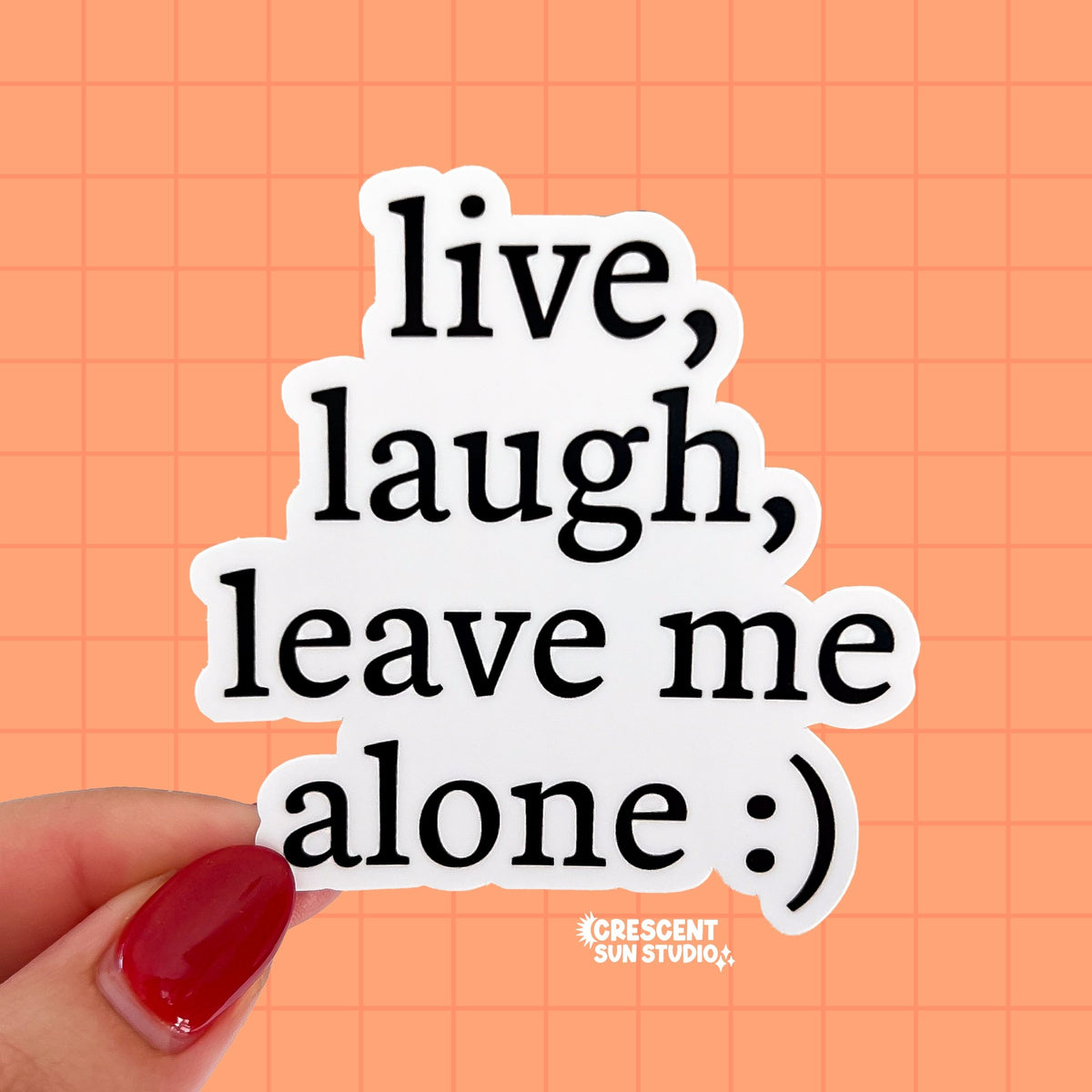 A die-cut sticker (follows the shape of the words) that reads "live, laugh, leave me alone" on four lines in black text on a white background. At the end of the text there is a smiley face emoticon. 