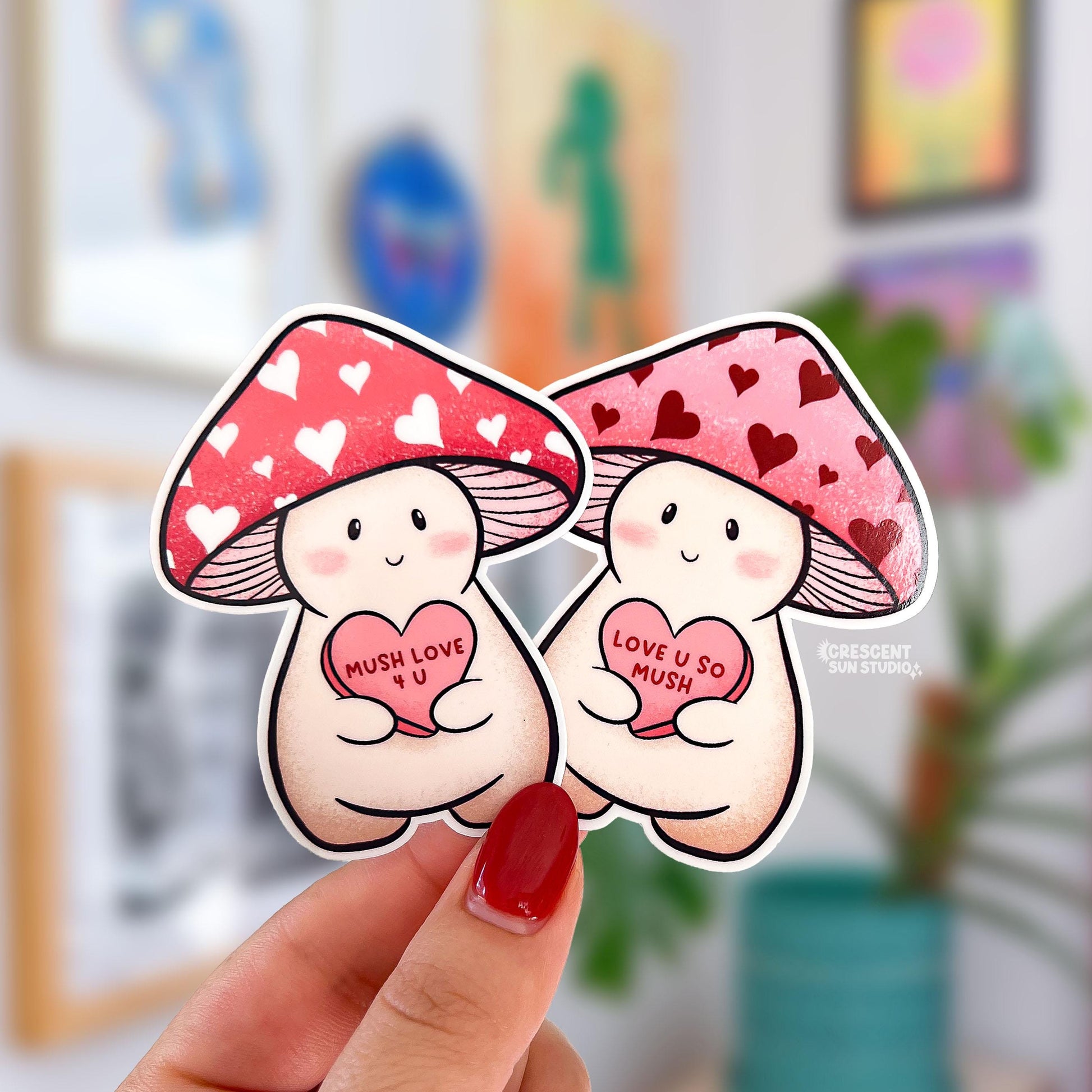 Two stickers of mushroom characters, one with a red cap with white hearts holds a candy heart that says "Mush Love 4 U." The other has a pink cap with red hearts and holds a candy heart that reads "love you so mush"