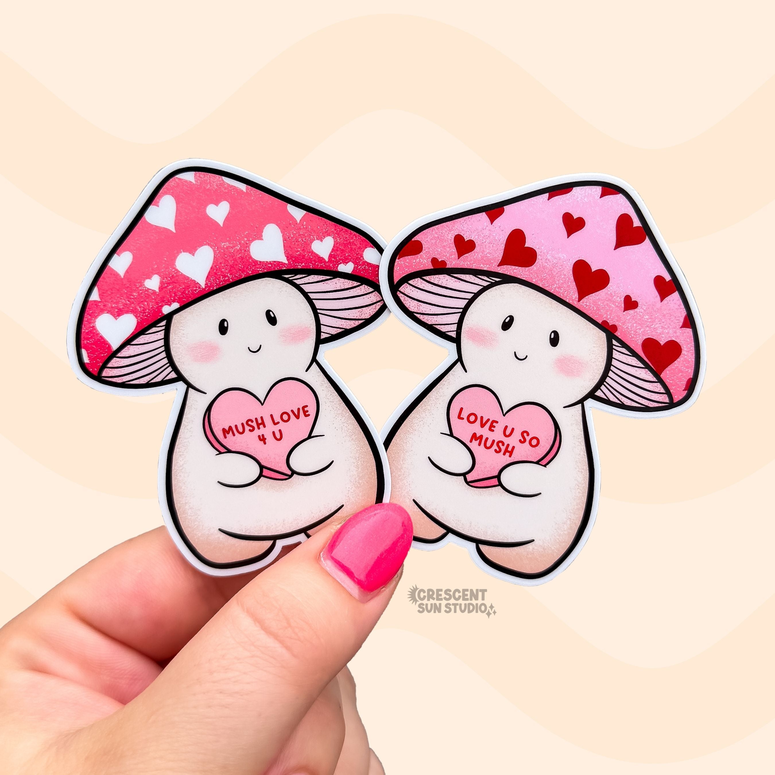 Two stickers of mushroom characters, one with a red cap with white hearts holds a candy heart that says "Mush Love 4 U." The other has a pink cap with red hearts and holds a candy heart that reads "love you so mush"