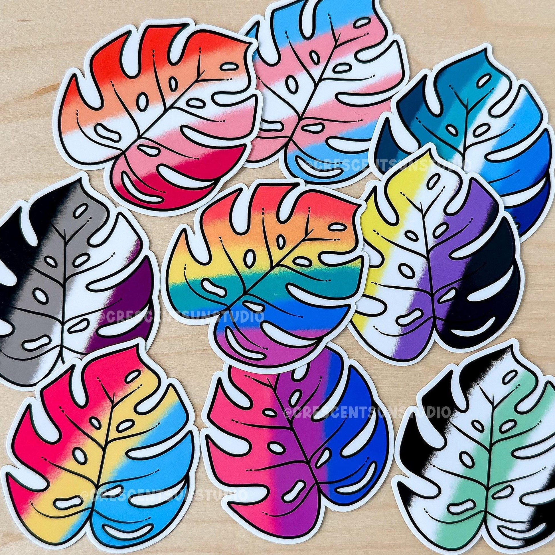 Colorful monstera leaf shaped stickers on a wooden surface.