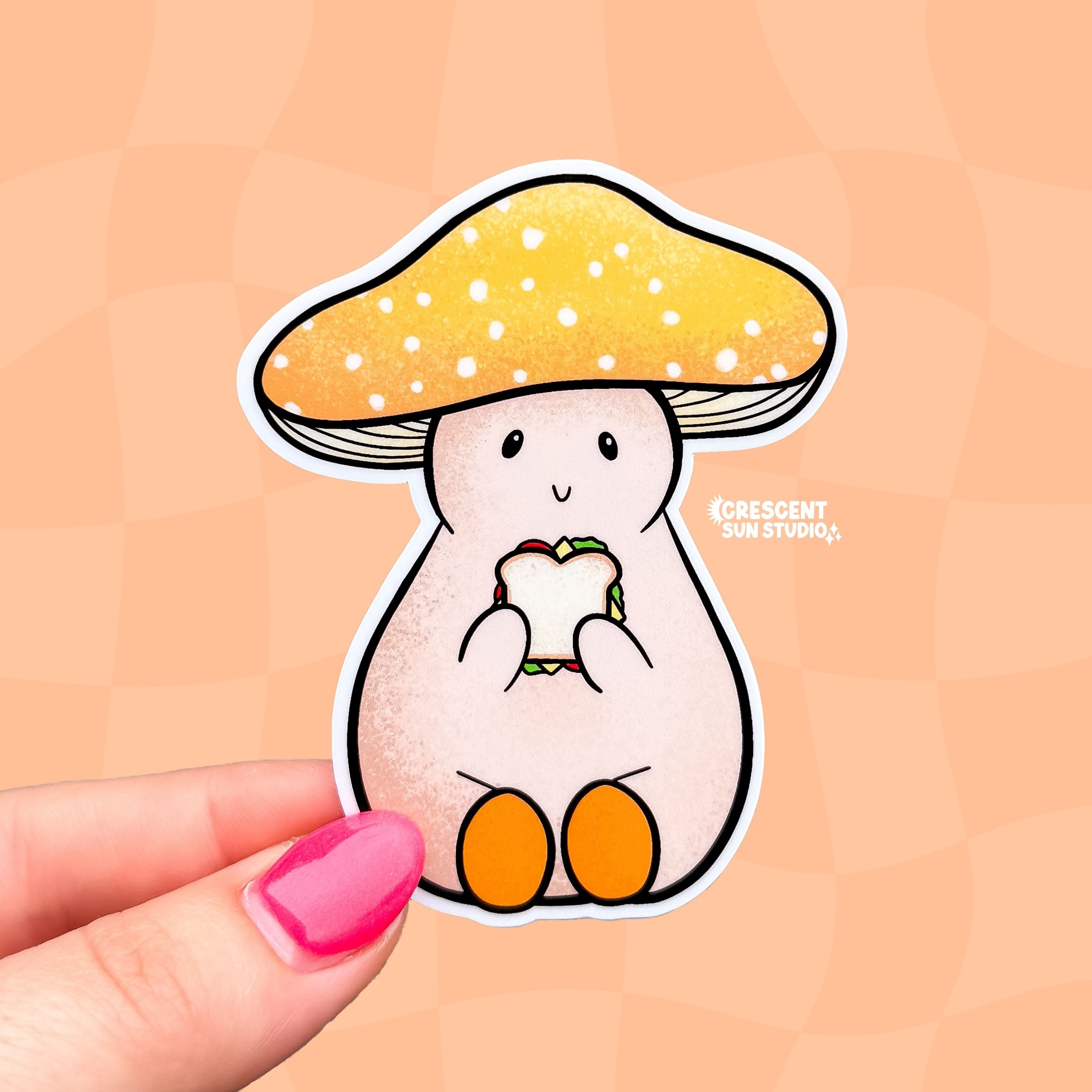 A die cut sticker of a pale mushroom character. His mushroom hate is a warm yellow with white spots. He is happily eating a sandwich. 