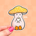 A die cut sticker of a pale mushroom character. His mushroom hate is a warm yellow with white spots. He is happily eating a sandwich. 