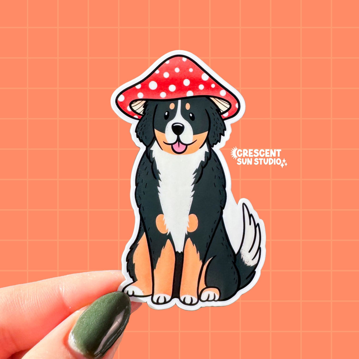 A die cut sticker of a fluffy Bernese mountain dog wearing a red and white mushroom cap for a hat. The dog has a silly expression and his tongue is sticking out.