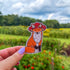A die cut sticker of an orange fox wearing a red mushroom cap. The mushroom hat has holes for the fox's ears to peek through.