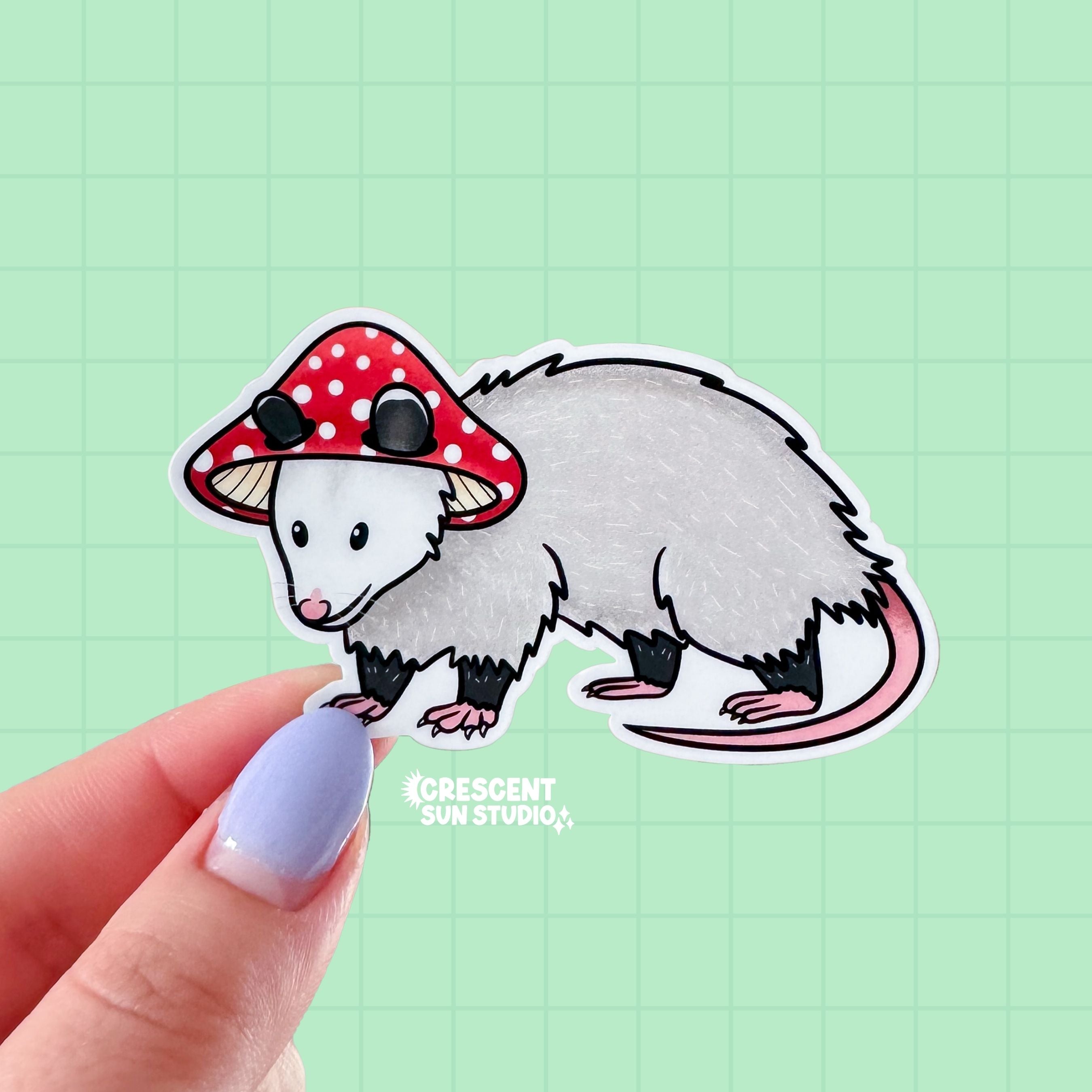 A die cut sticker of an opossum wearing a red and white mushroom cap for a hat.