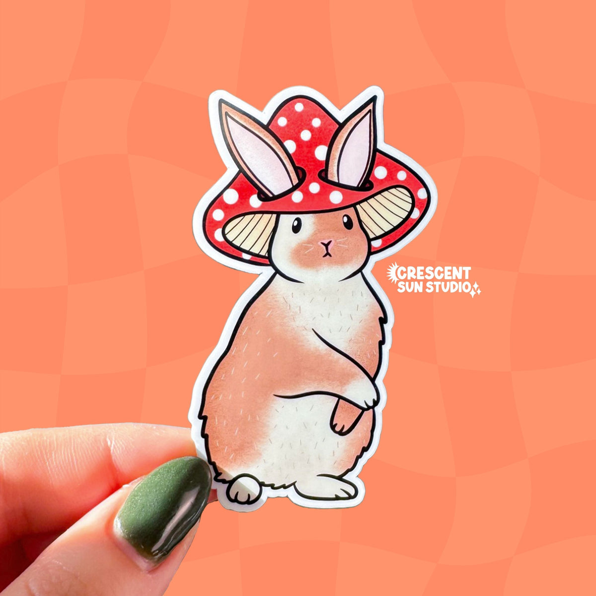 Die-cut sticker of a fluffy brown and white rabbit wearing a red spotted mushroom cap, standing upright with a composed expression.