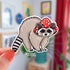A diecut sticker of an adorable raccoon wearing a red mushroom cap.