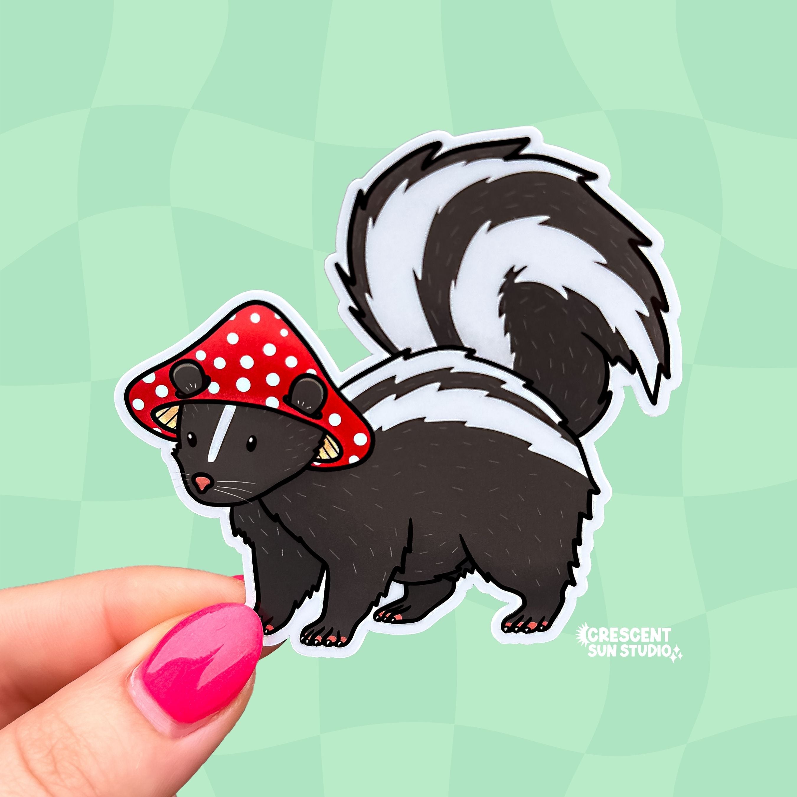 A die cut sticker of a skunk wearing a red and white mushroom cap for a hat.