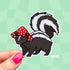 A die cut sticker of a skunk wearing a red and white mushroom cap for a hat.