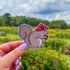 A zoomed out image of a die cut sticker of a squirrel wearing a red mushroom cap and holding an acorn.