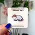 A small enamel pin in the shape of an opossum wearing a red and white mushroom hat. The pin is displayed on a light colored card.