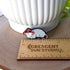A small enamel pin in the shape of an opossum wearing a red and white mushroom hat. In this image, the pin is next to a ruler showing its width of 1.35 inches.