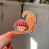 The cat is a tabby (orange with darker orange stripes) and has a sweet expression on his face. His red mushroom hat with white spots has spots for his ears to poke through. The cat is in a stretching pose with his tail curling up behind him.

In this image, the cat-shaped sticker is held close to the camera.
