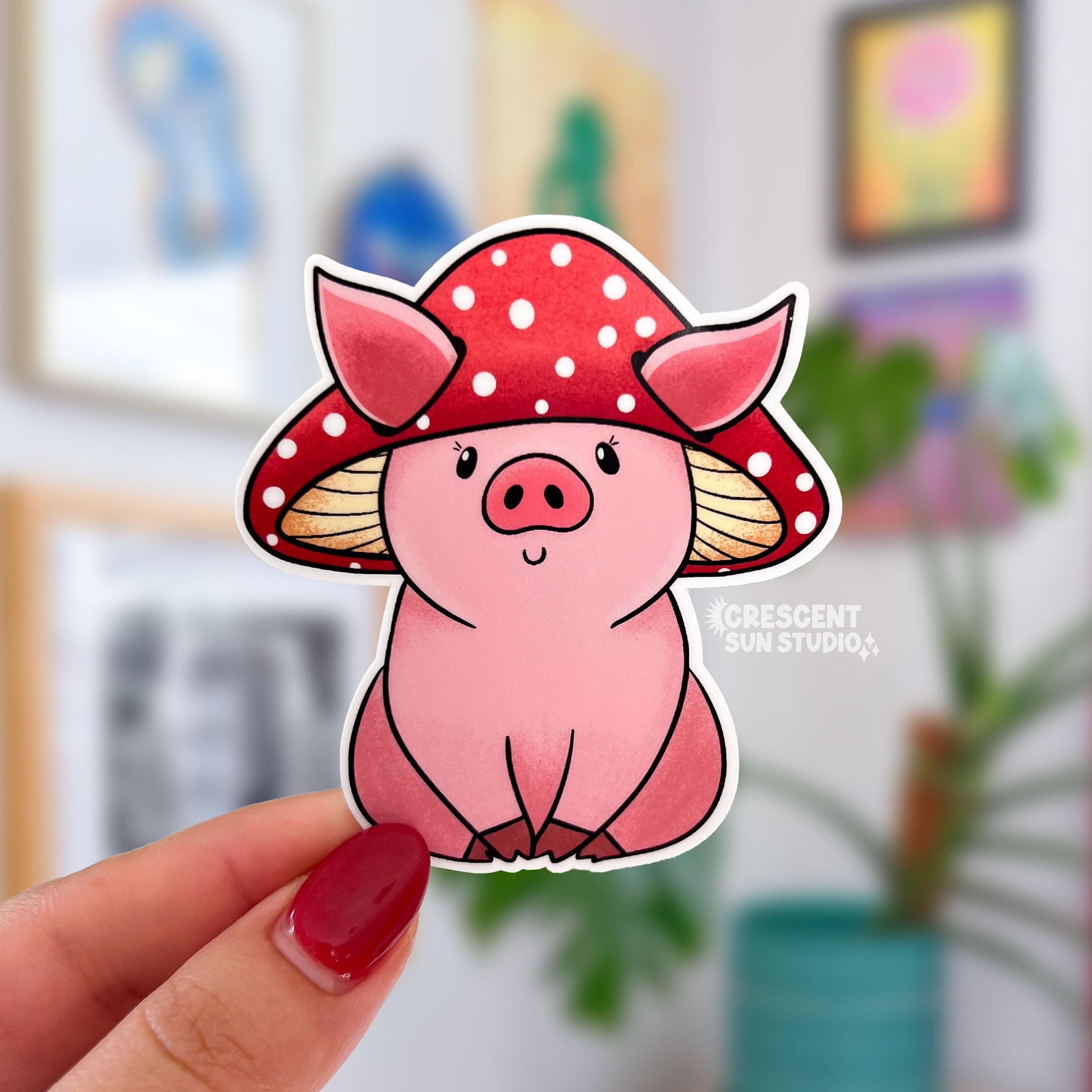 A sticker in the shape of a sitting pig wearing a mushroom hat. This pink shaded pig happily wears a red mushroom with white spots as a hat. His large pig ears stick out of the mushroom.