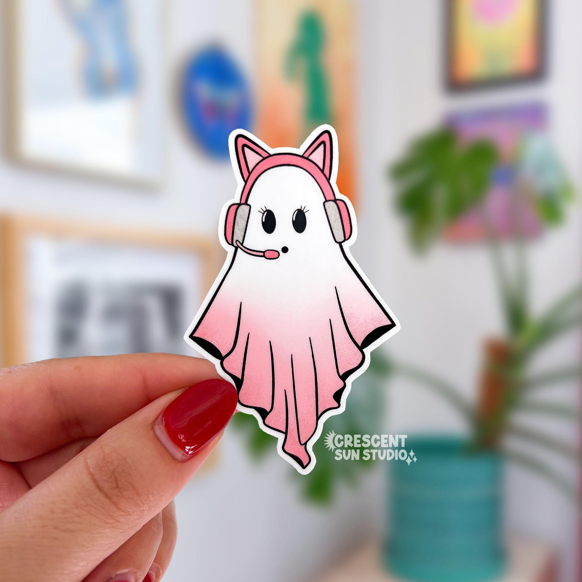 A sticker in the shape of a ghost wearing a pink cat ear headseat. Her body is in gradient pink and you can tell she is involved in an intense conversation