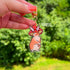 Acrylic die cut of a fluffy brown and white rabbit wearing a red spotted mushroom cap, standing upright with a composed expression. Keychain has a gold u-shaped clasp.