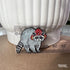 This enamel pin features a gray raccoon with a striped tail. The raccoon is wearing a red mushroom cap with white spots. The cap has little holes for the raccoon's ears to poke through.

A clear plastic ruler sits in front of the pin, showing its size of 1.35 inches.