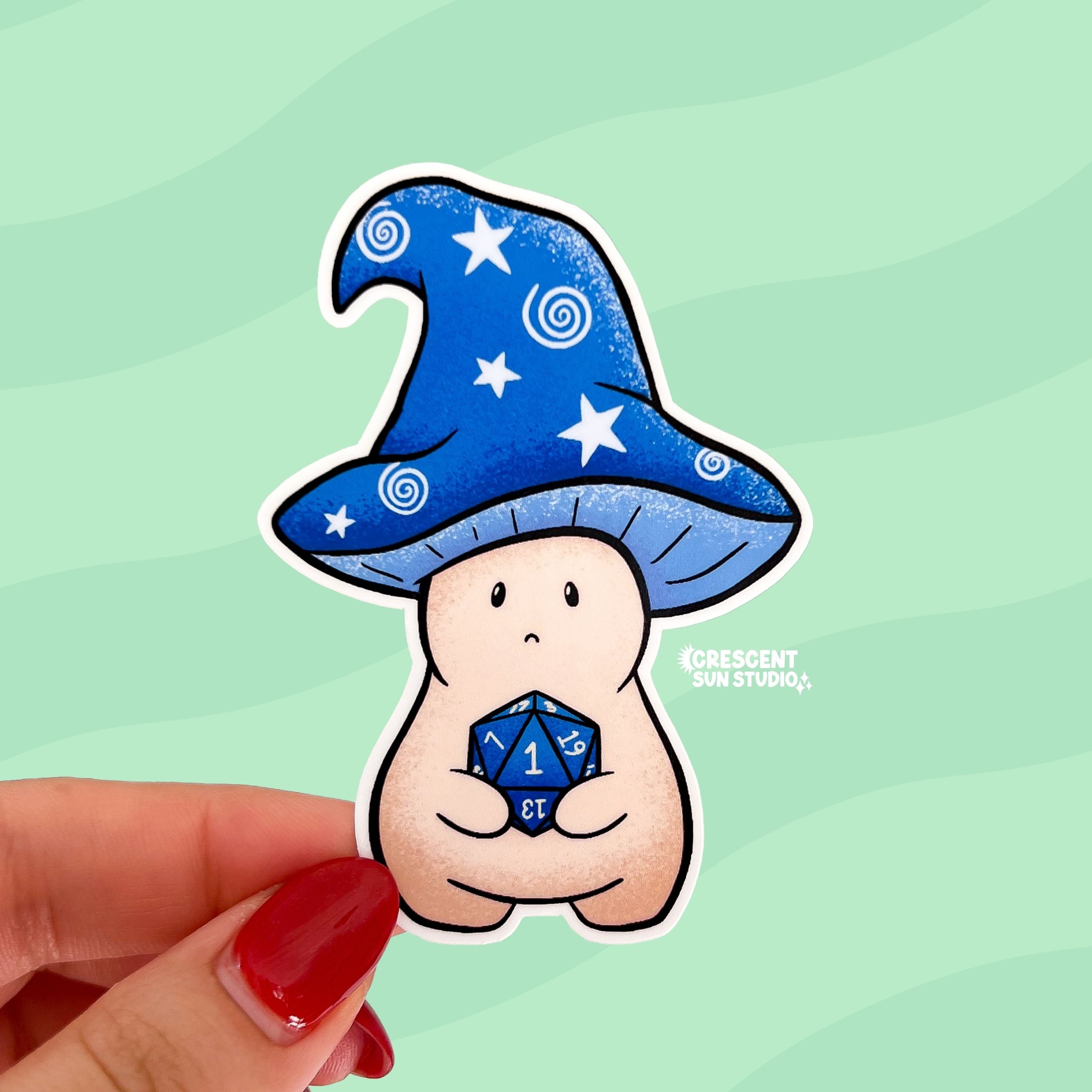 A sticker in the shape of a wizard mushroom character. The mushroom cap is blue with white stars and spirals. The magician holds a 20-sided die, used in tabletop games, and has rolled a 1.