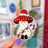 A die-cut sticker of a mushroom wearing a santa hat on top of his red and white spotted cap. The mushroom is a pinky-beige color, has a smile on his face, and his holding a giant candy cane.