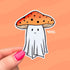A sticker in the shape of a ghost wearing an orange mushroom top for a hat. The mushroom has dark dots on it and the ghostie has a smiling face.