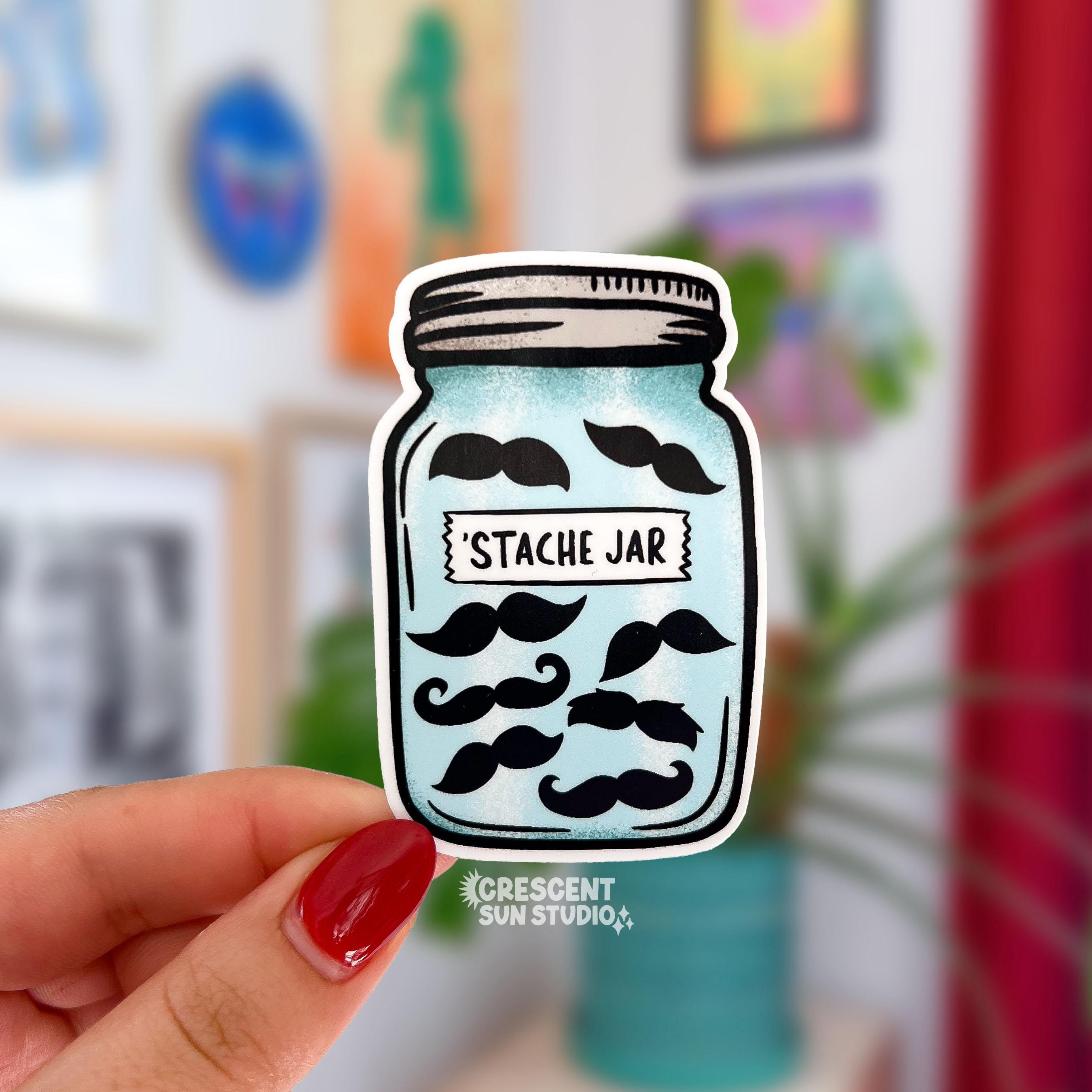A mason jar shaped sticker full of various shaped black mustaches has a "stache jar" label on it