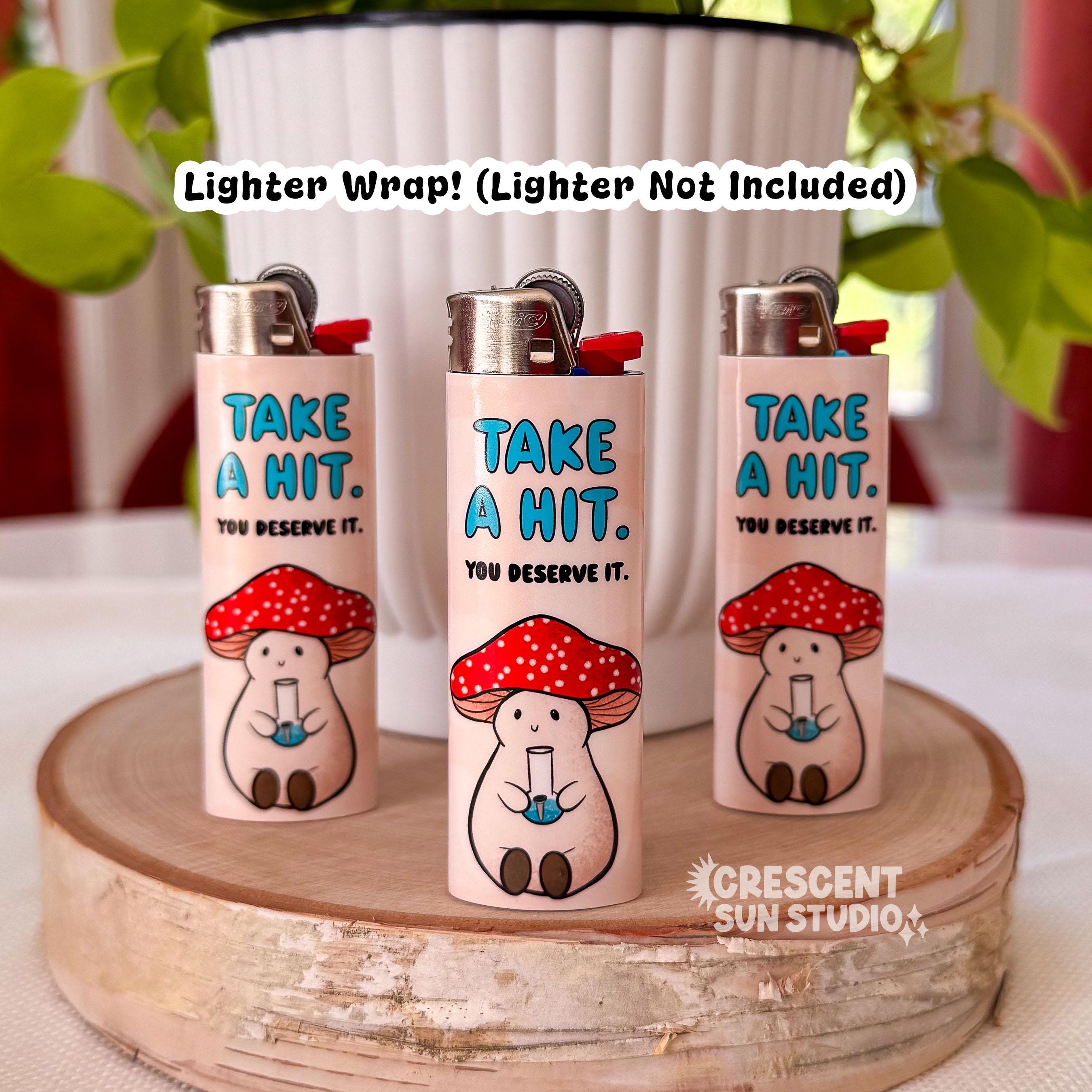 Three lighters stand on display, each wrapped in a peachy-beige lighter wrap. On the top of the wrap in blue letters it reads, "take a hit" and below that it says "you deserve it." At the bottom of the wrap sits Stoney the Mushroom, our pinky-beige plump mushroom character with a red and white spotted cap is joyfully holding a bong in his little mushroom hands.

Across the top of the image in black text, it reads: Lighter wrap! Lighter not included"