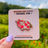 A small enamel pin of a pink cow with darker pink spots has two strawberries at the top of her head, as if they were horns, as well as a strawberry at the end of her tail. The pin is displayed on a light pink card.