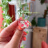A small enamel pin of a pink cow with darker pink spots has two strawberries at the top of her head, as if they were horns, as well as a strawberry at the end of her tail. The pin is displayed on a light pink card.