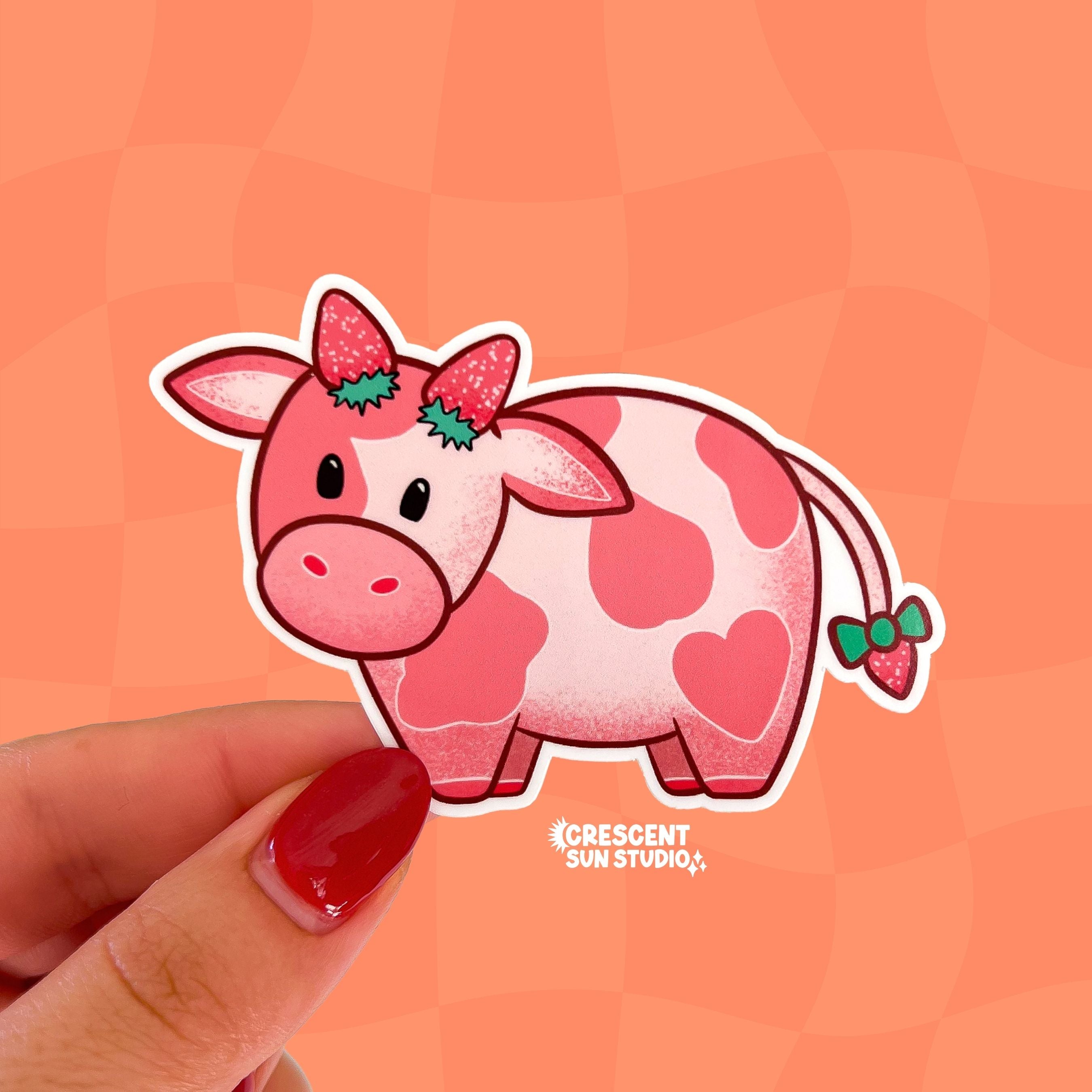 A pink cow with darker pink spots has two strawberries at the top of her head, as if they were horns, as well as a strawberry at the end of her tail.