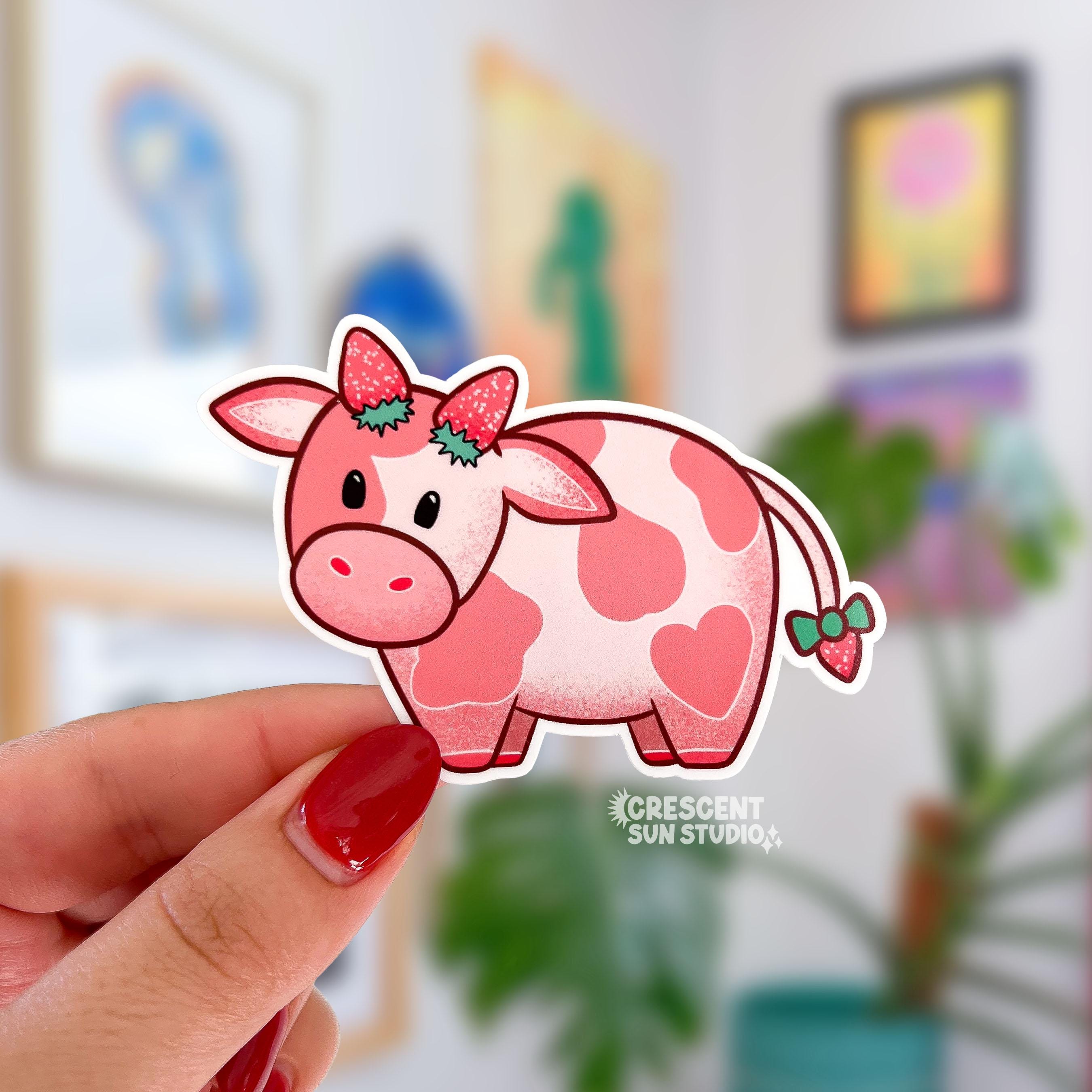 A pink cow with darker pink spots has two strawberries at the top of her head, as if they were horns, as well as a strawberry at the end of her tail.