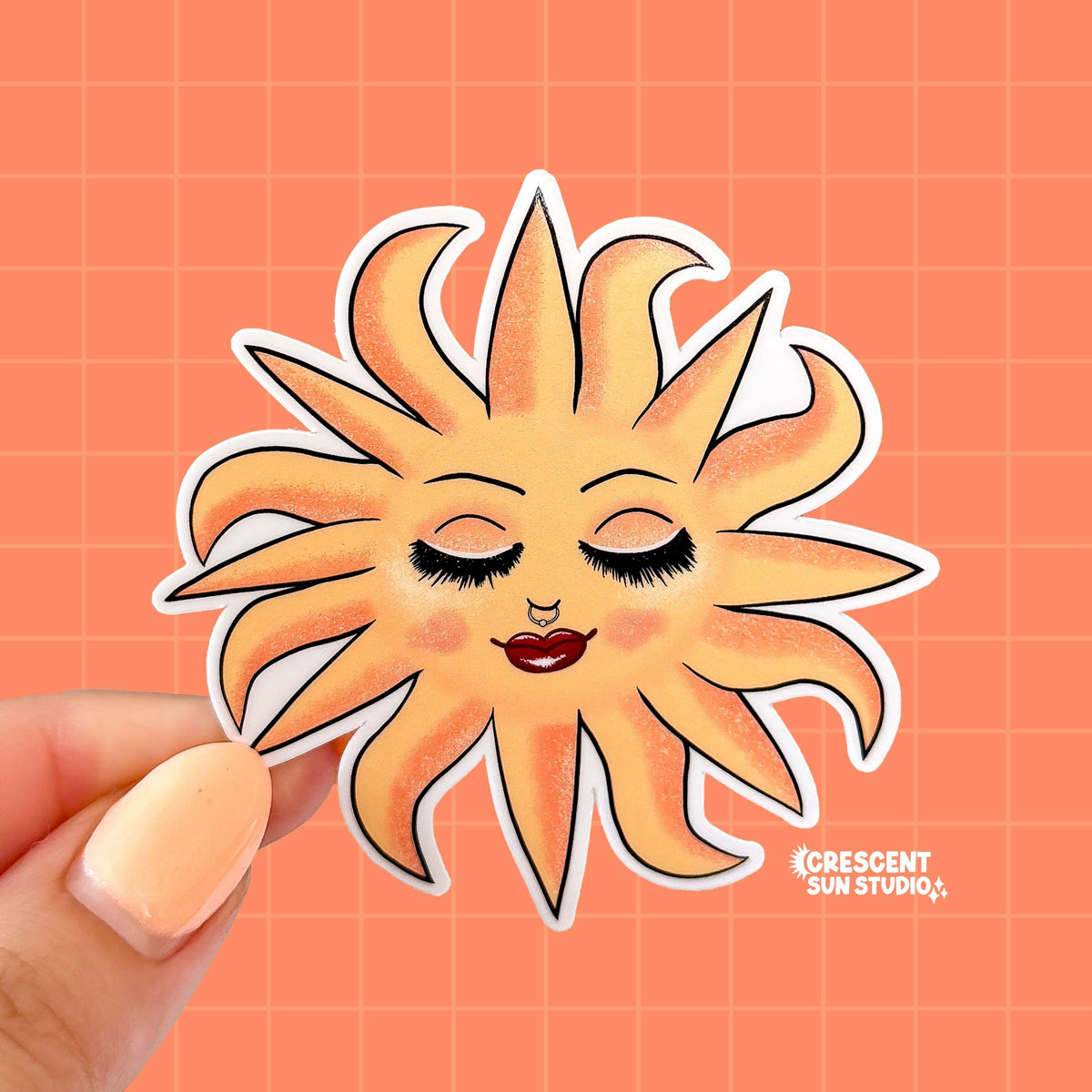 This sticker features a blissed out and glam sun with rays of light dancing around her. This personified sun has thin eyebrows, closed eyes with full lashes and eyeshadow, a nose ring, blushing cheeks, and glossy full lips.