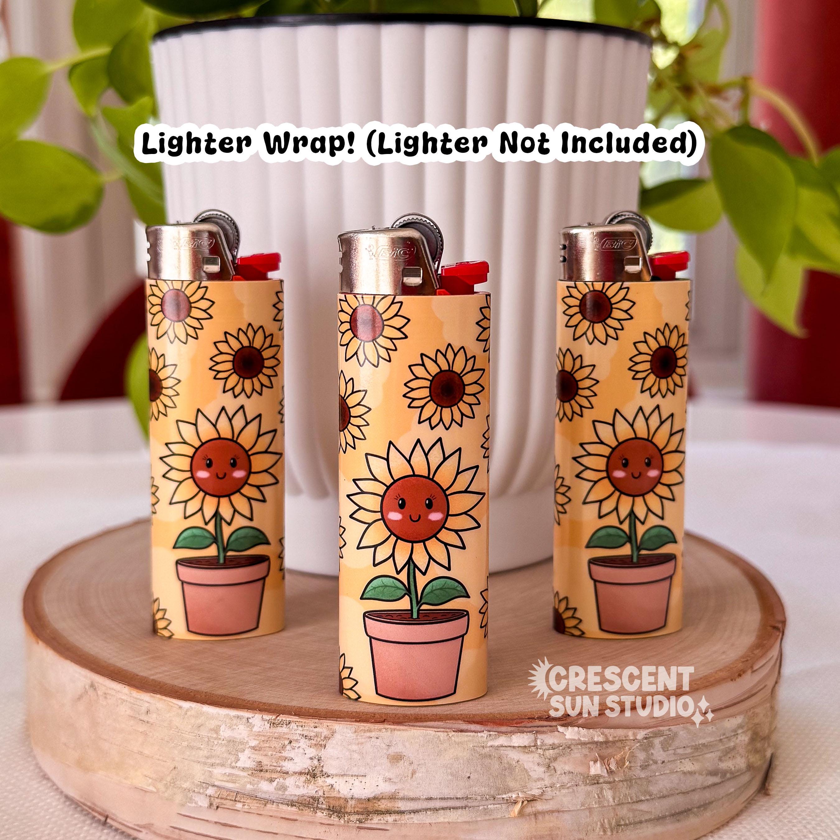 Image depicts three yellow lighters. The pattern on the lighters is a background of yellow and brown sunflowers, in the foreground is a happy sunflower character with pink cheeks and a smiling face. She is in a terracotta pot.

The text on top of the image reads: Lighter Wrap! Lighter not included.
