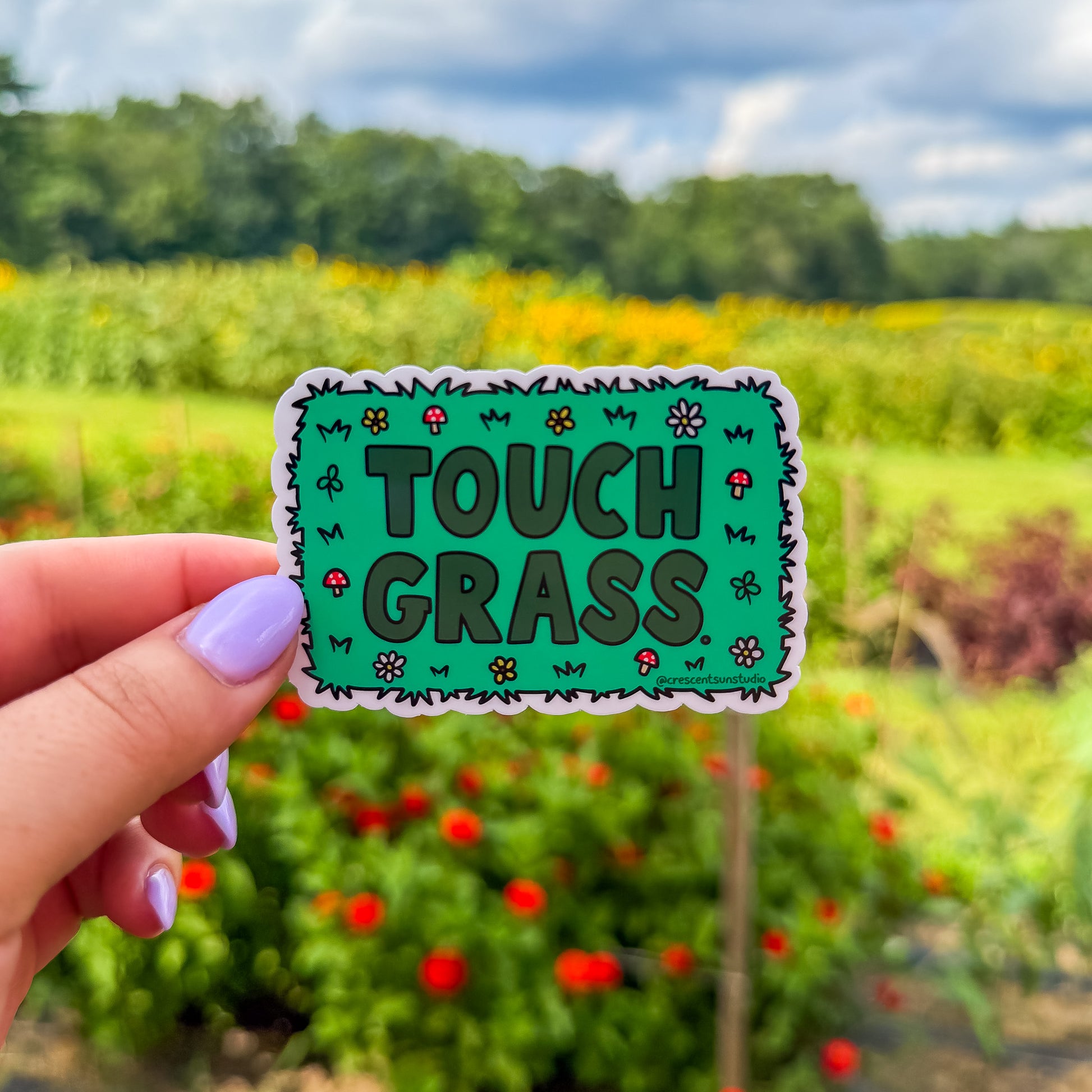 Green sticker with darker green text that reads "touch grass." The words are surrounded by mushroom and flower doodles.