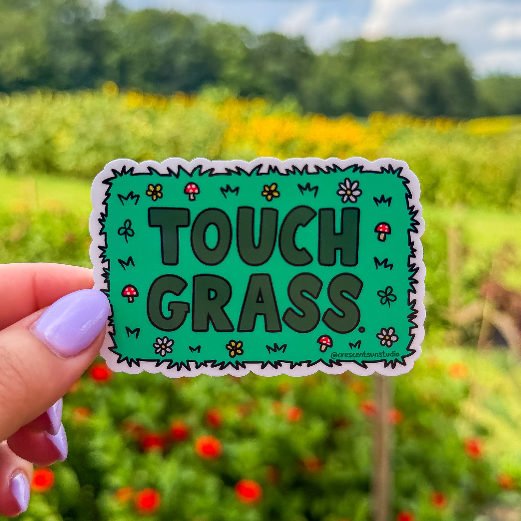 Green sticker with darker green text that reads "touch grass." The words are surrounded by mushroom and flower doodles.