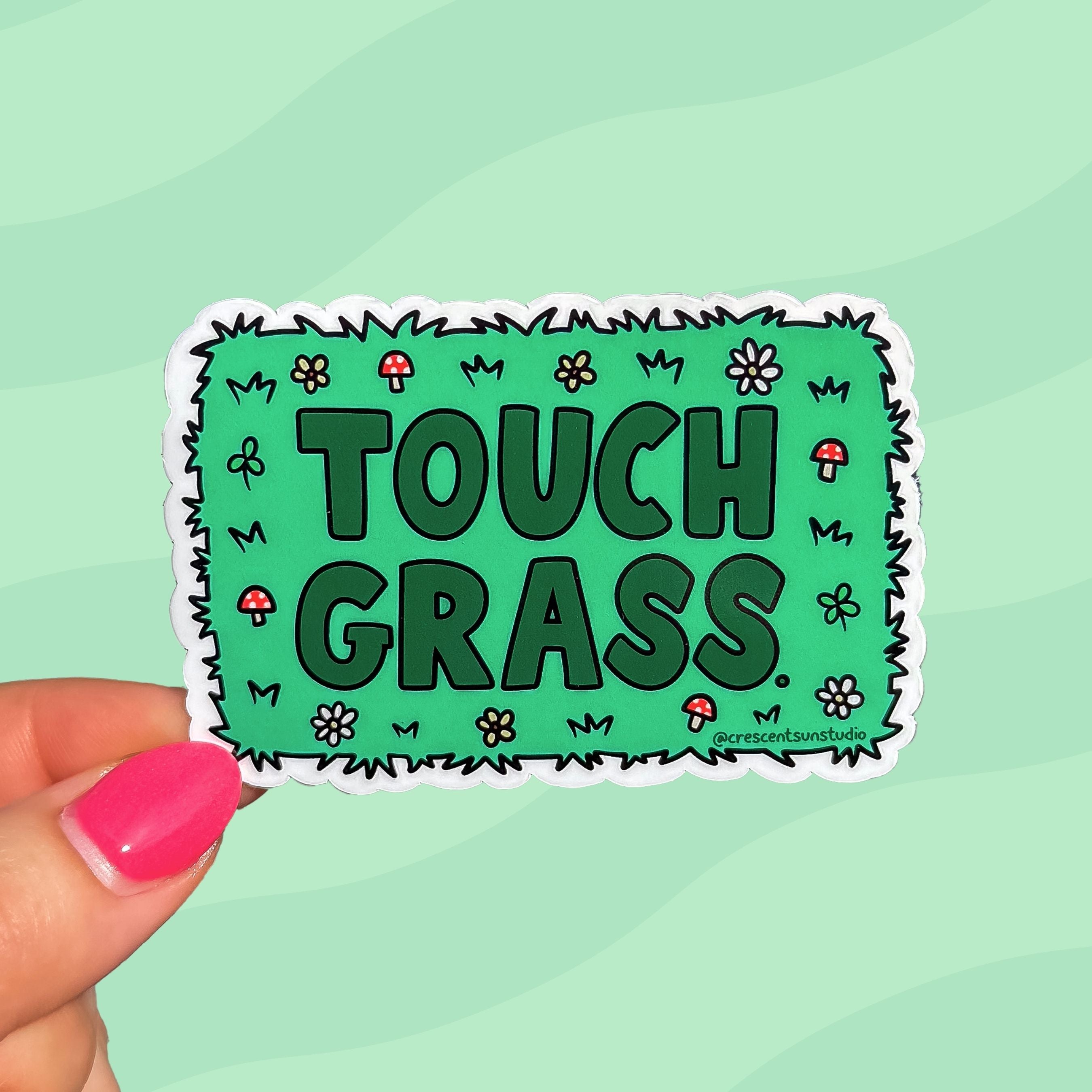 Green sticker with darker green text that reads "touch grass." The words are surrounded by mushroom and flower doodles.