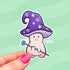 A sticker in the shape of a mushroom with an oversized mushroom cap that hooks to one side. The happy beige mushroom is holding a want with a crystal and moon on one end. His hat is purple with stars and spirals.