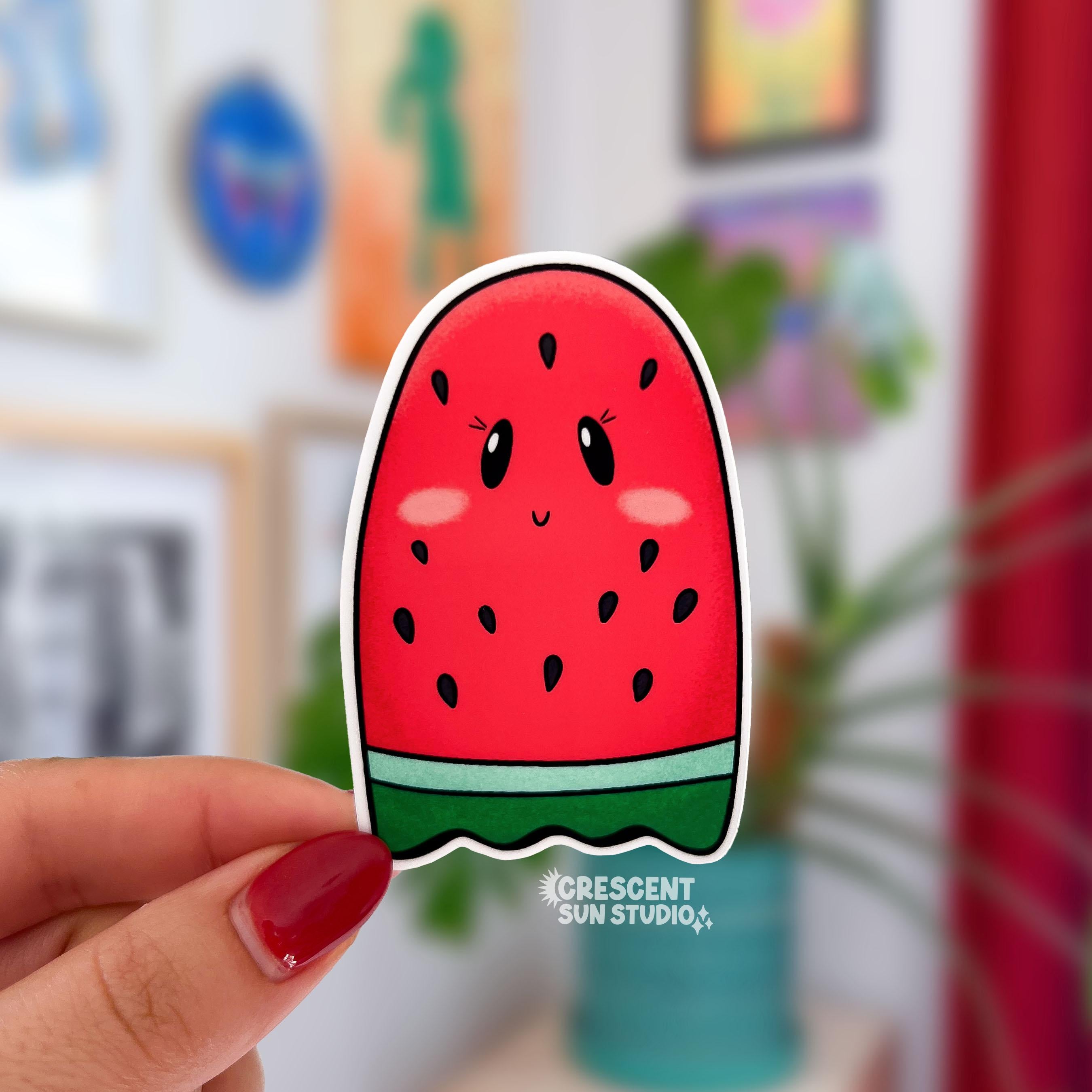 A sticker that looks like a red seeded watermelon slice shaped like a ghost is held close to the camera.