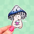 A sticker cut in the shape of a happy little mushroom character. Her mushroom cap is shaded blue-black with dark moons and stars on it. The bottom of the cap has little drips, resembling ink. She is holding a potion bottle with pink liquid inside.