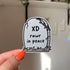 a die cut gravestone sticker with the epitaph "XD rawr in peace"