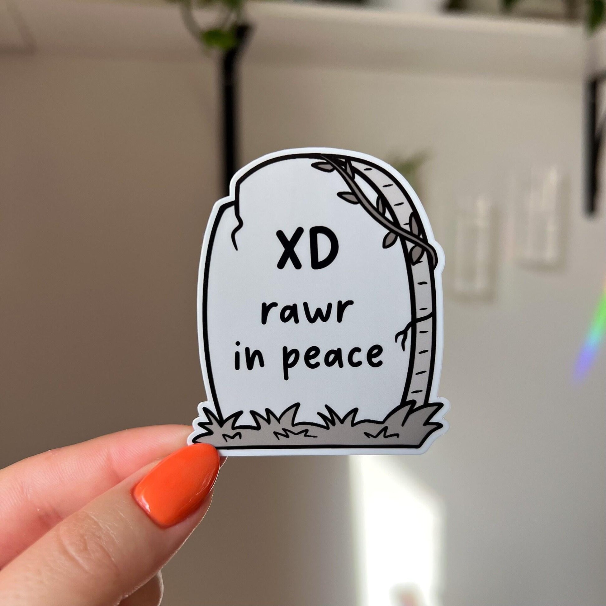 a die cut gravestone sticker with the epitaph "XD rawr in peace"